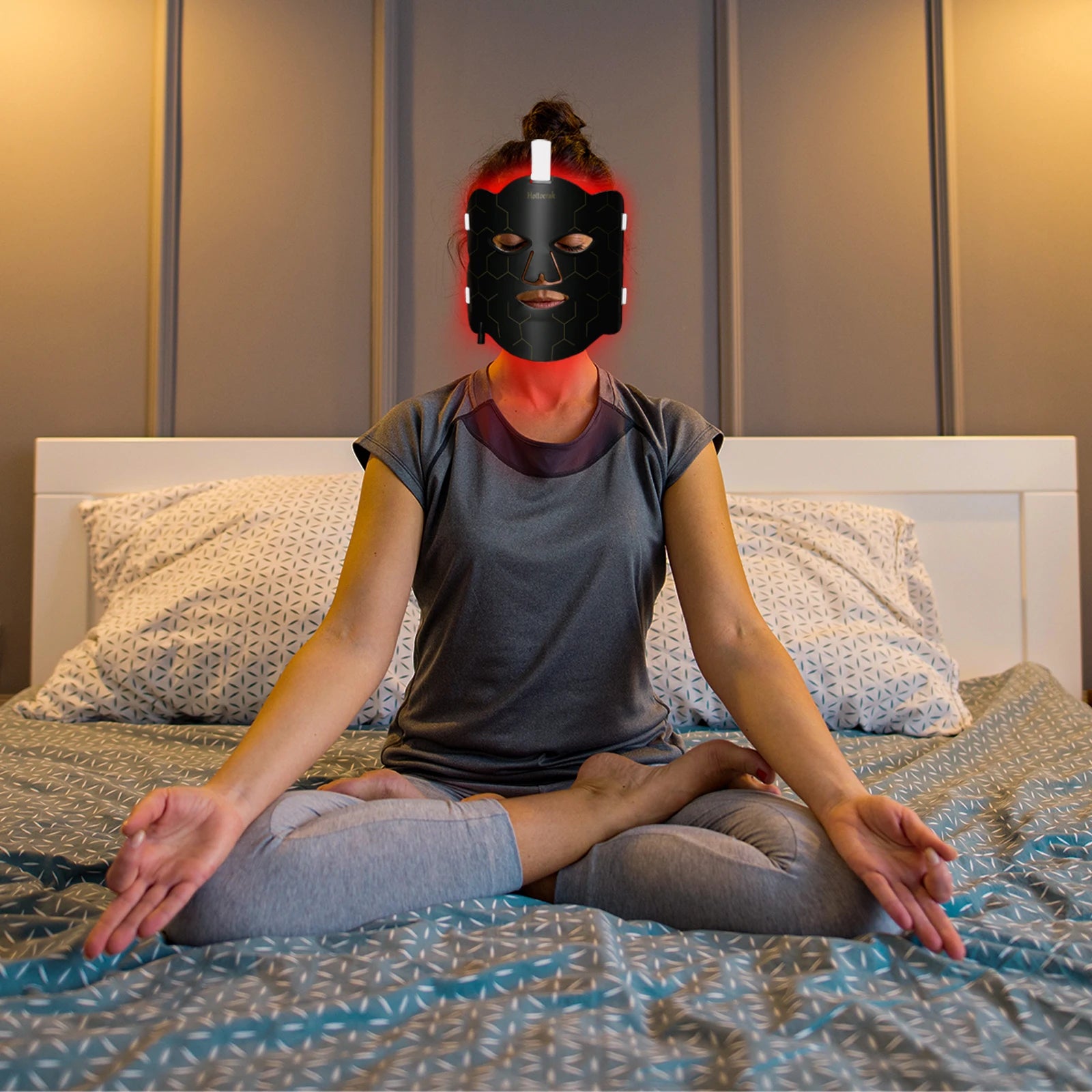 Woman wearing a black flexible silicone LED red light therapy mask for facial and neck skin care while meditating.