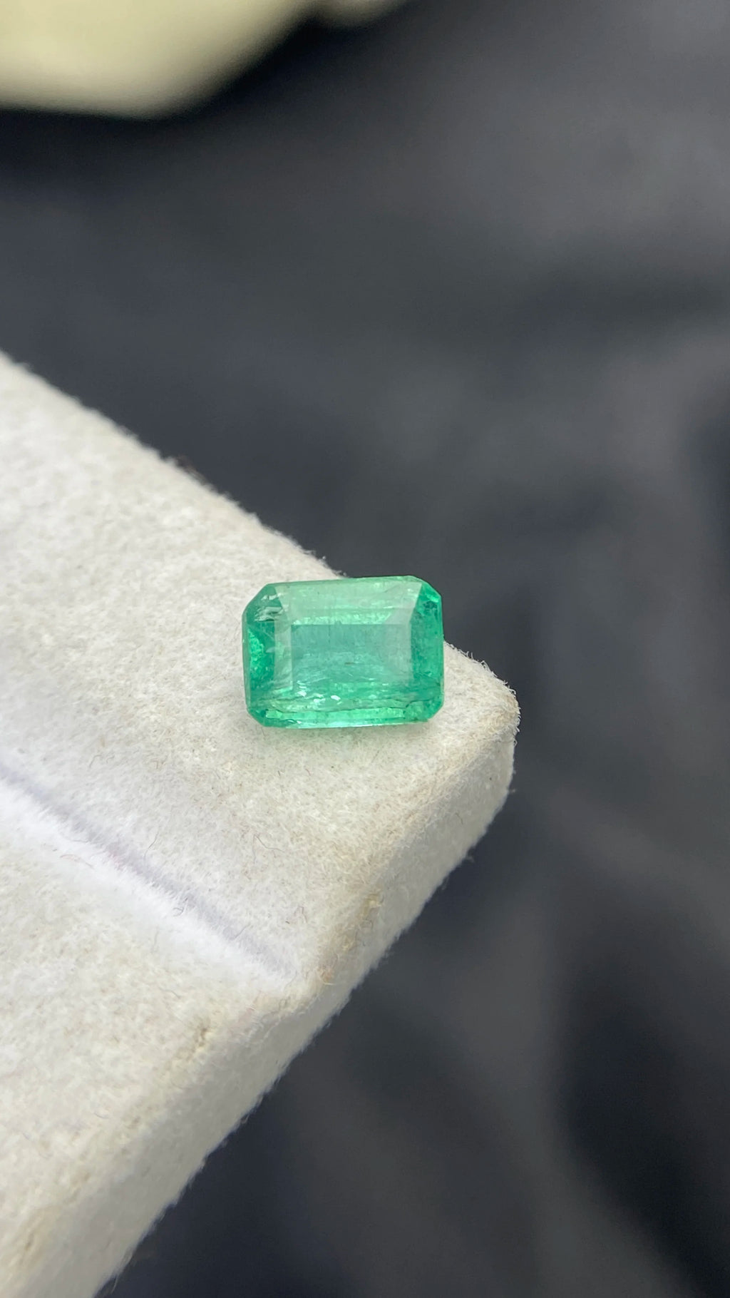 Loose emerald-cut green gemstone with step facets, on white felt pad