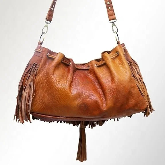 Tan leather bucket shoulder bag featuring bohemian fringe detailing, a drawstring closure, and a detachable strap.
