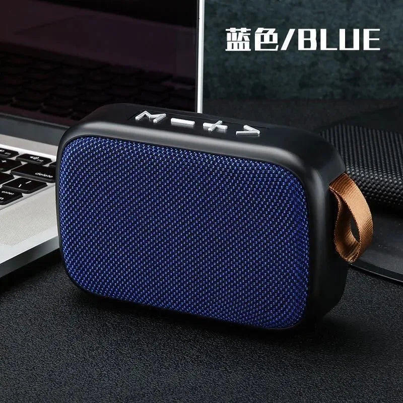 Tidesmit rectangular blue fabric and black plastic Bluetooth speaker with a tan carry strap next to a laptop.