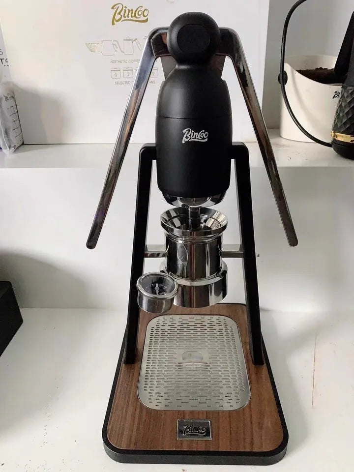 Binco manual espresso maker with black frame, chrome piston, and wood base on a drip tray with pressure gauge.