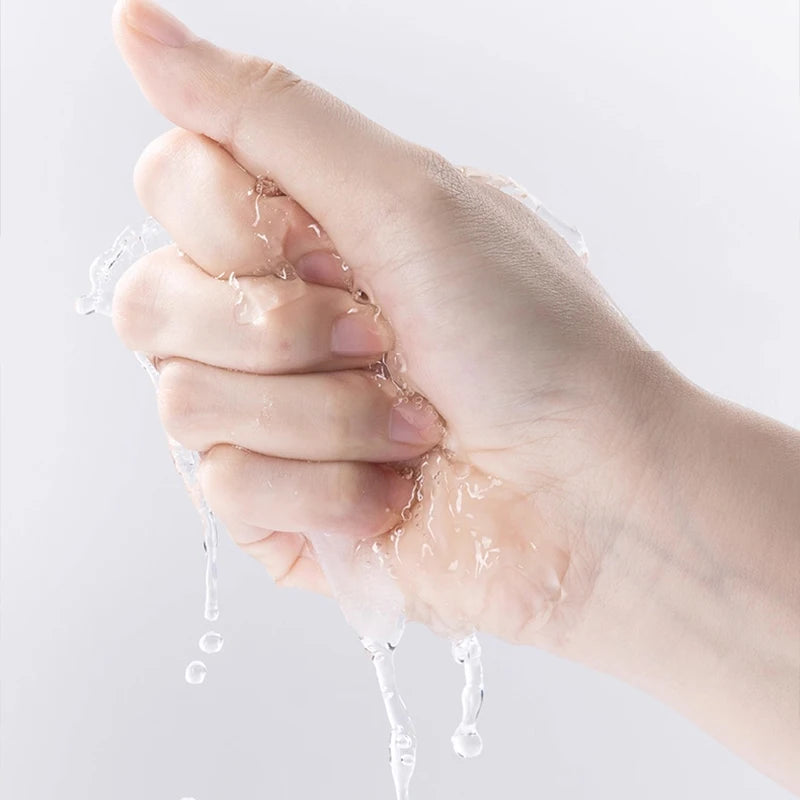 A hand holds and squeezes a thin, wet, white facial mask sheet, with water dripping from it.