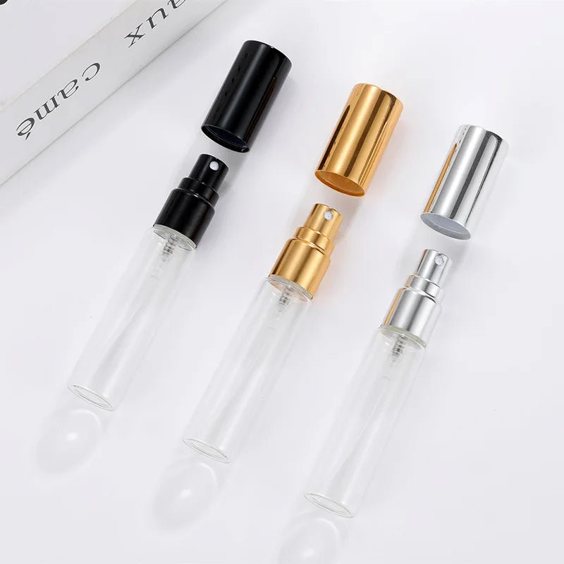 Three slim, cylindrical glass perfume spray bottles with black, gold, and silver caps and pump misters.