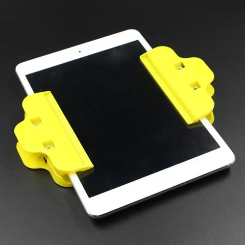 Two yellow plastic Tidesmit clip-style clamps secured to the sides of a white tablet screen for repair.