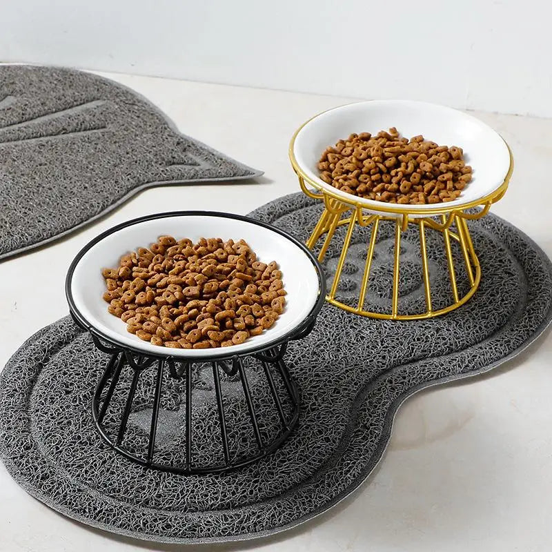 Raised ceramic pet bowls with gold and black metal stands for ergonomic cat or dog feeding on a grey mat.