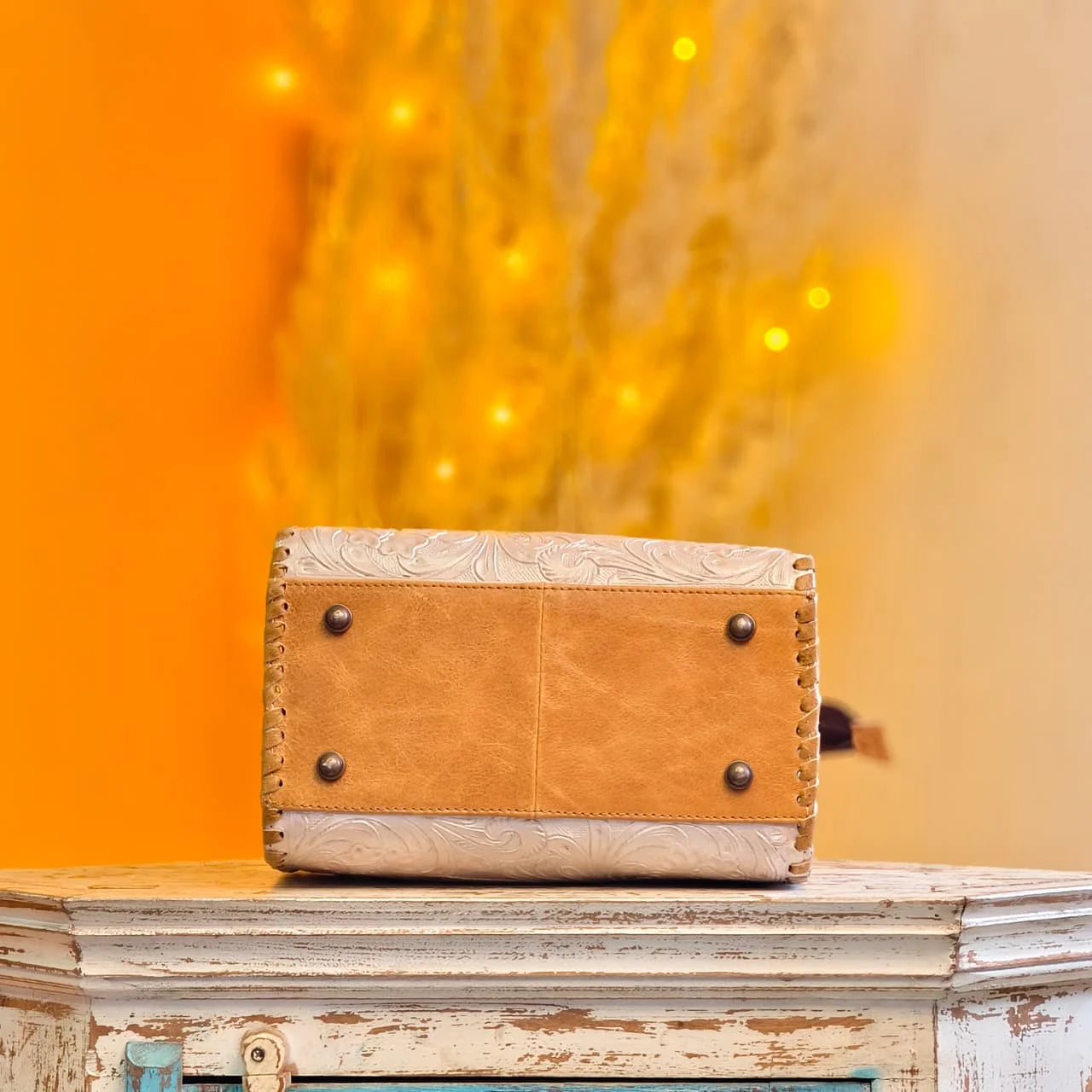 Tan and cream genuine leather mini duffel with floral tooling, side stitching, and metal base feet. Designer handbag.