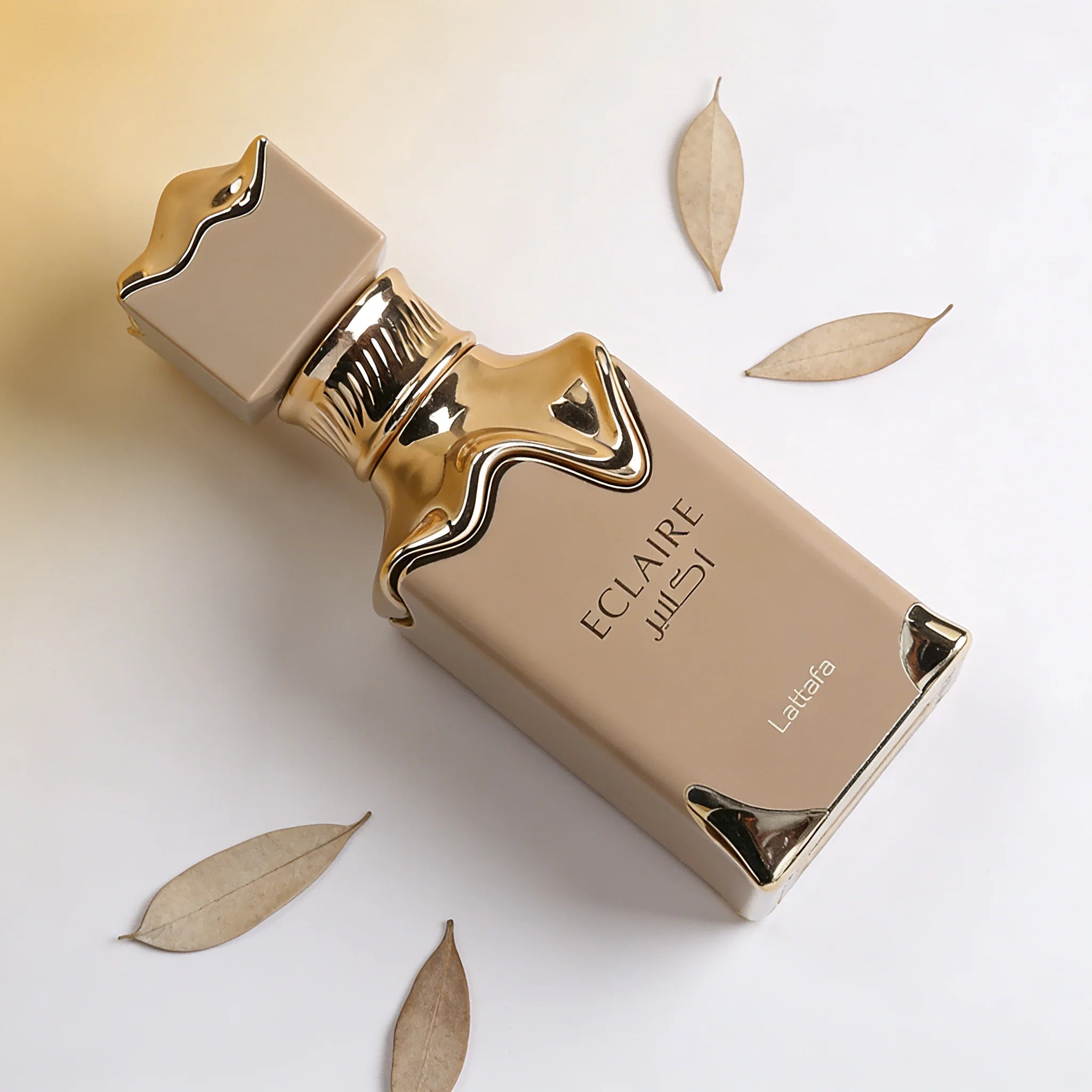 Lattafa Eclaire perfume bottle in beige matte finish with gold metallic accents and crown cap on a white background.