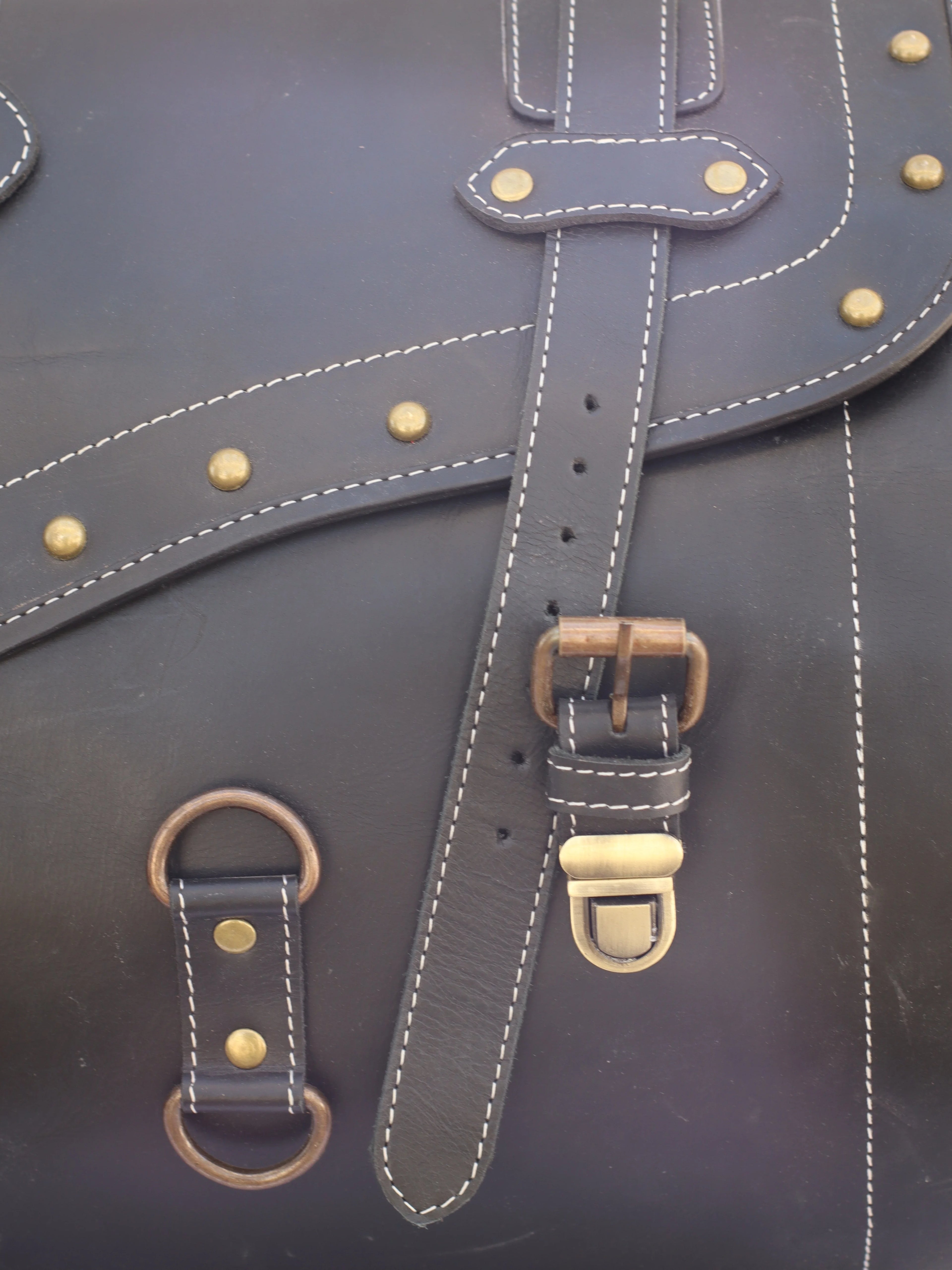 Black leather trunk luggage featuring vintage brass studs, contrast stitching, and metal buckle closures.