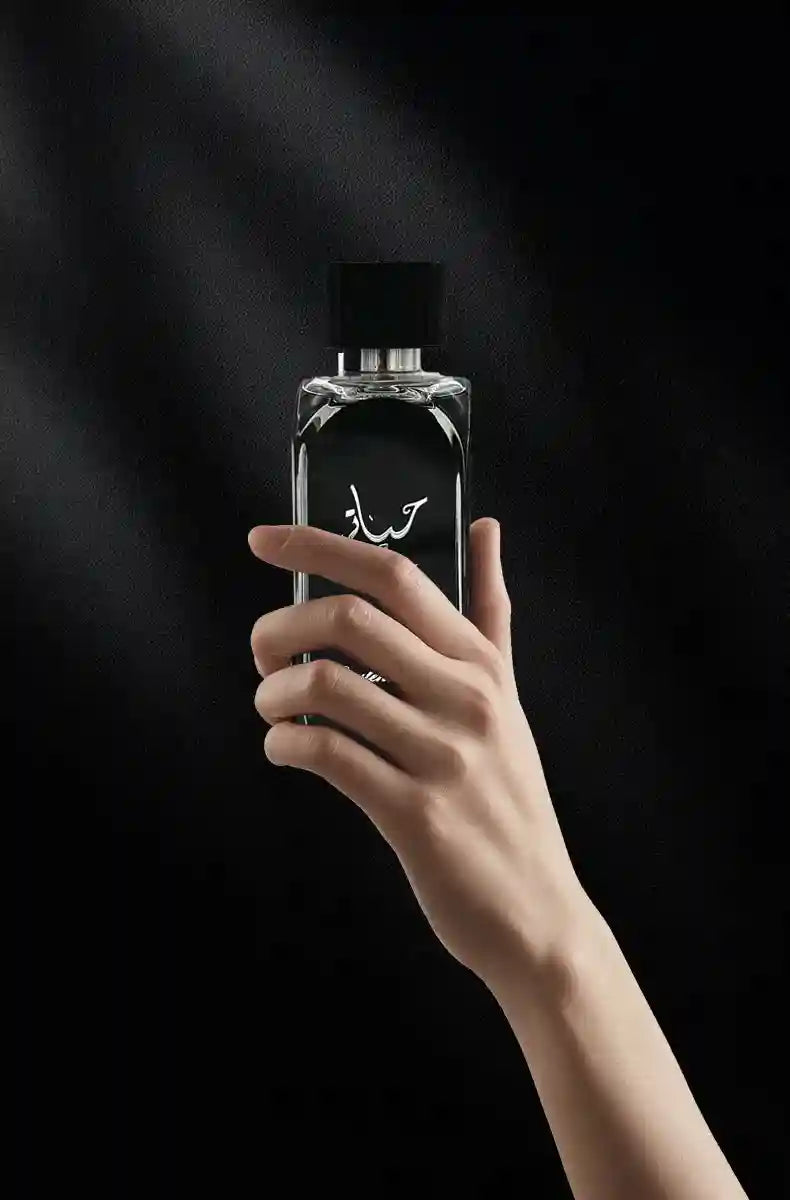 Hand holding a black rectangular bottle of long-lasting Middle Eastern Arabic aromatic perfume for men in a gift box.