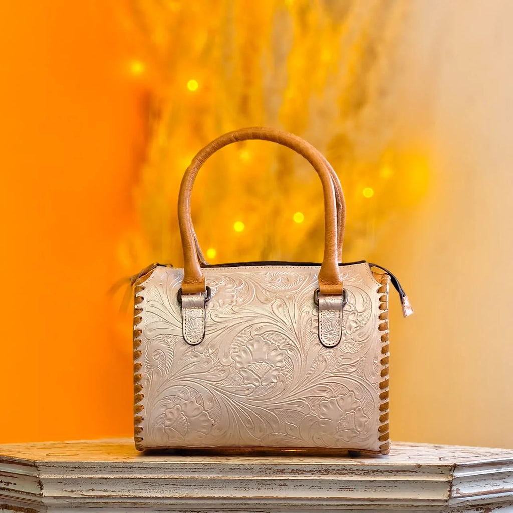 White leather mini speedy duffel bag with floral hand-tooling, whipstitch sides, and tan handles. Designer handbag.