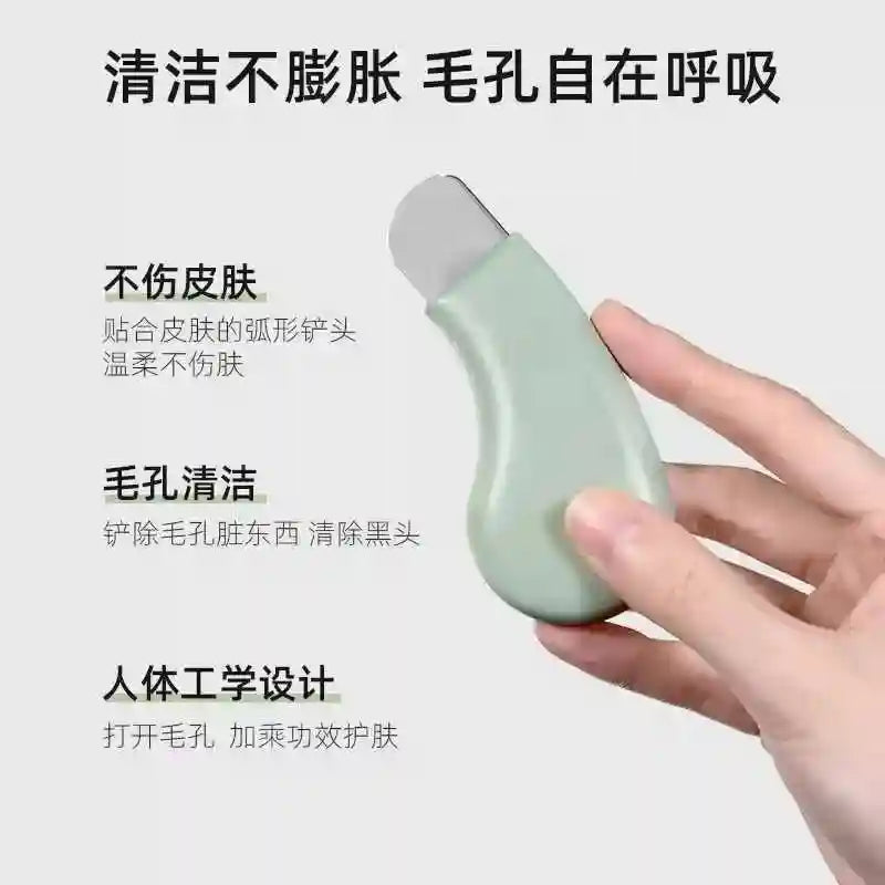 Hand holding a sage green, ergonomic blackhead removal tool with a metallic, curved spatula tip for pore cleaning.