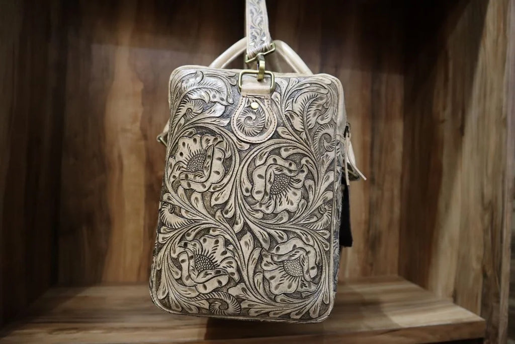 Handmade vintage brown cowhide leather travel duffel with intricate western floral tooling and antique brass hardware.
