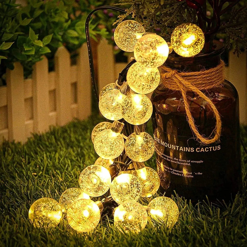 Solar bubble ball LED string lights with warm glowing round bulbs draped on outdoor hedge.