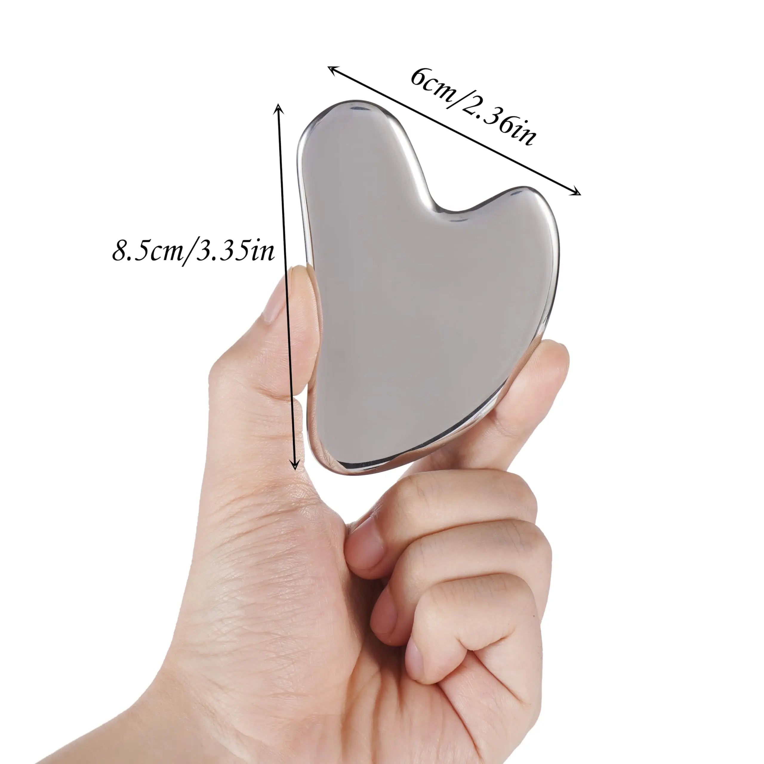 A hand holds a heart-shaped, polished silver stainless steel Gua Sha facial massage tool with size measurements.