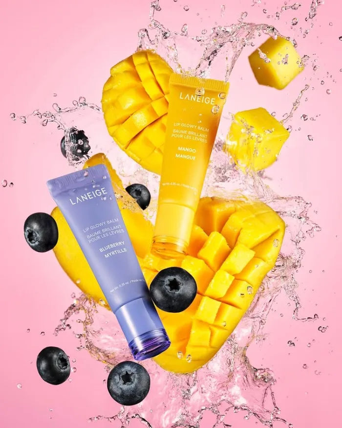 Laneige Lip Glowy Balm set: Blueberry and Mango tubes with fresh fruit and water splashes on a pink background.