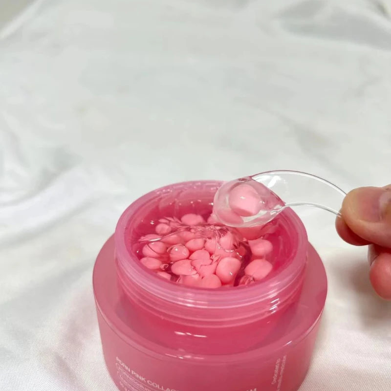 A pink jar filled with clear gel and small pink capsules, being scooped with a clear plastic spatula.