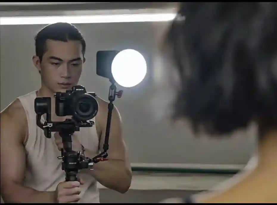 Camera gimbal with a mounted circular LED light and mirrorless camera, held by a man for stable video recording.