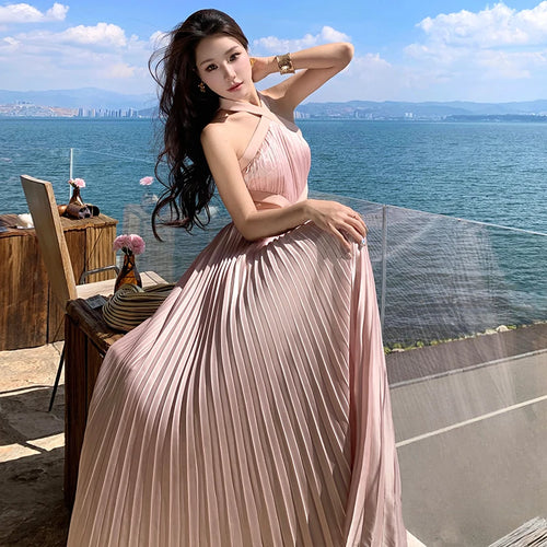 Tidesmit dusty pink sleeveless halter maxi dress with a pleated skirt, posing on a balcony overlooking the ocean.