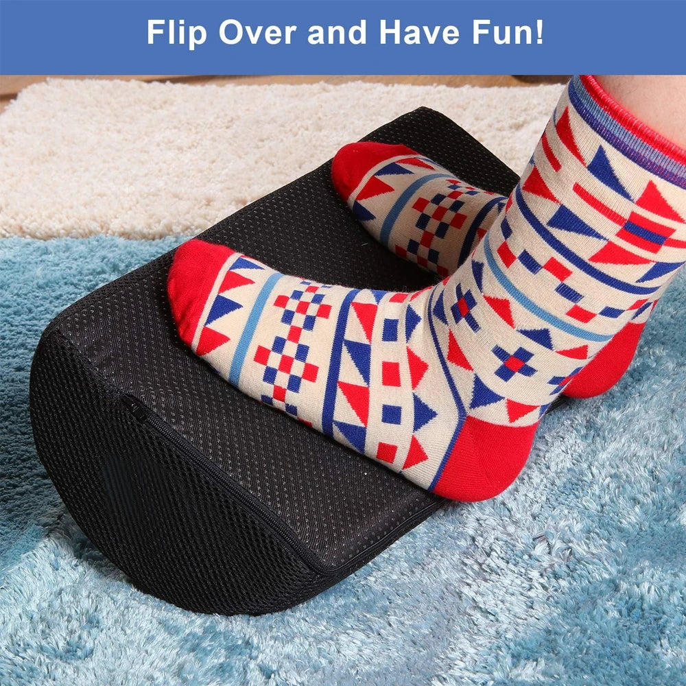 Black memory foam under desk foot rest with removable cover, supporting feet on a textured office desk floor cushion.