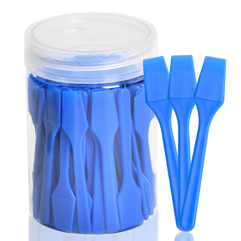A clear plastic jar filled with 100 blue, mini plastic cosmetic spatulas for skincare application.