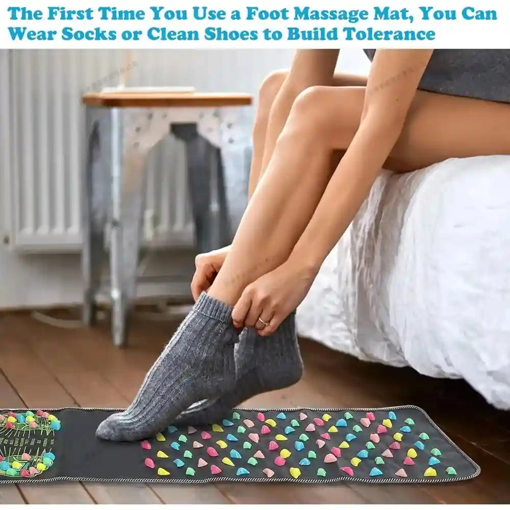 Person using a black reflexology foot massage mat with colorful acupressure stones for home pain relief.