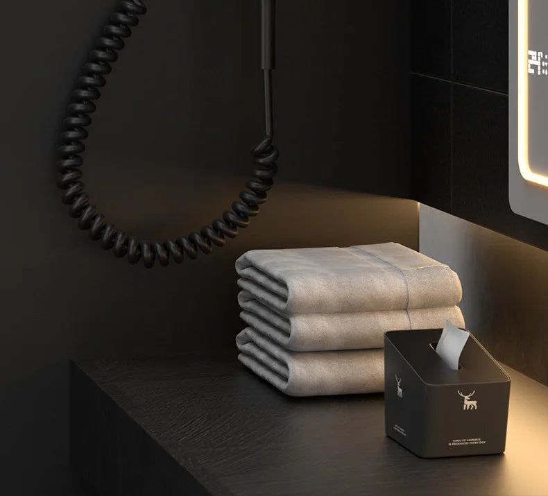 Modern matte black wall-mounted hotel hair dryer with coiled cord in luxury bathroom setting.