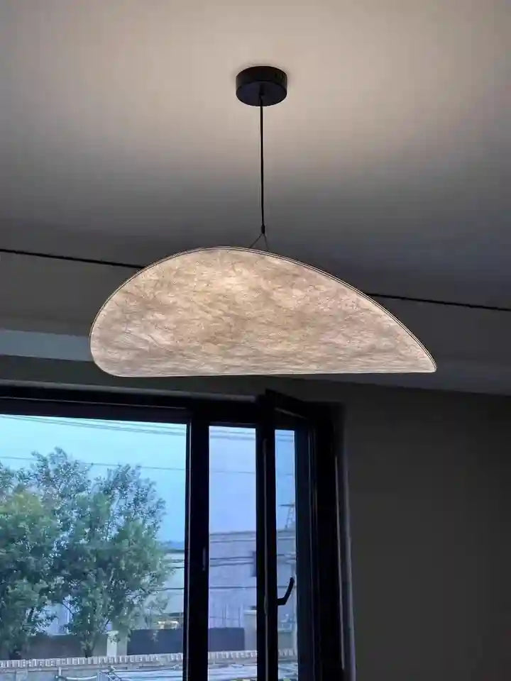 Large, crescent-shaped pendant light with a textured, cream-colored paper shade for ambient ceiling lighting.