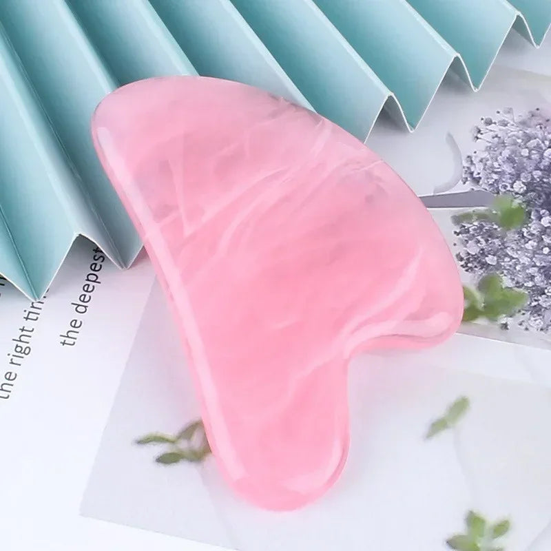 Heart-shaped pink resin gua sha massage tool with a smooth, marbled texture, resting on decorative paper.