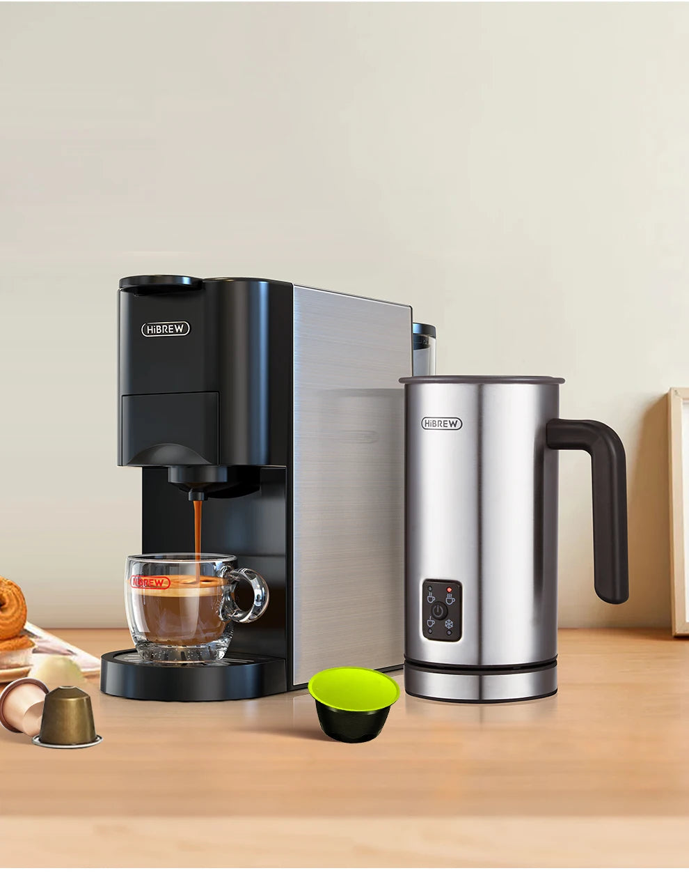 HiBREW stainless steel capsule coffee maker and matching electric milk frother brewing espresso into a glass cup.