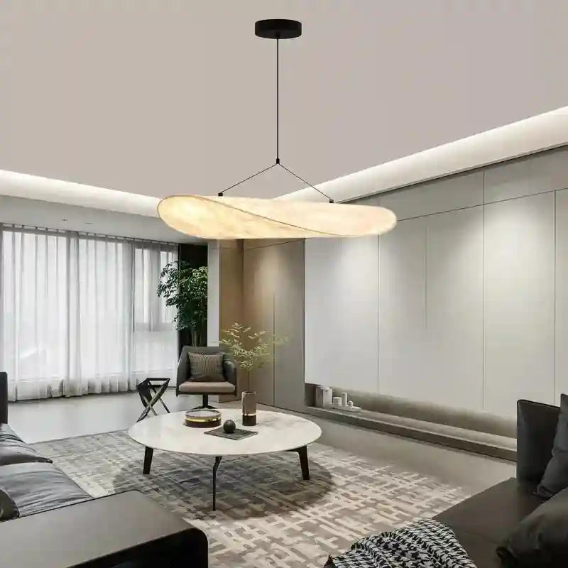 Oval pendant light with a textured, cream-colored fabric shade suspended by thin wires above a living room coffee table.