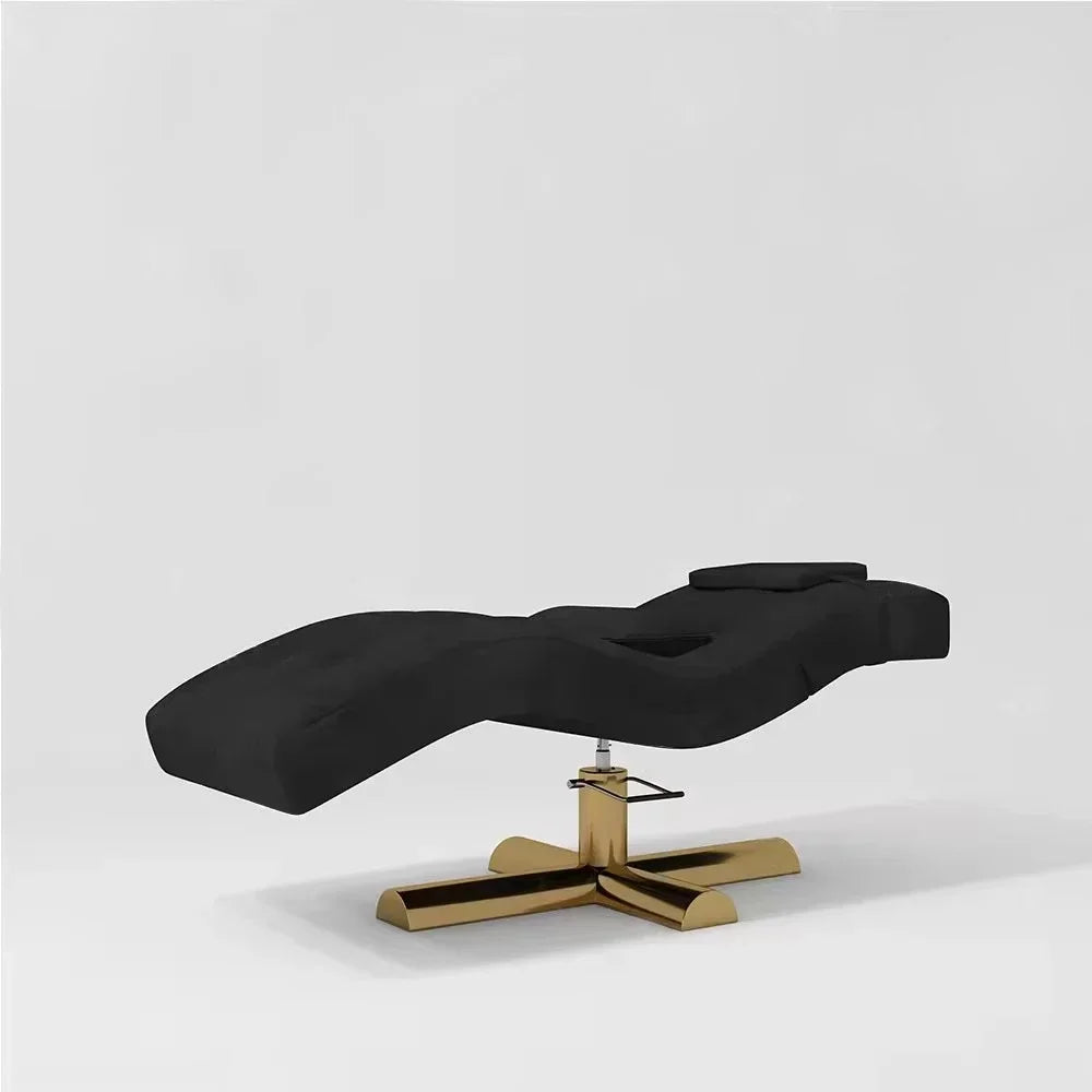 Black lash bed with a contoured cushion and gold pedestal base for professional salon services.