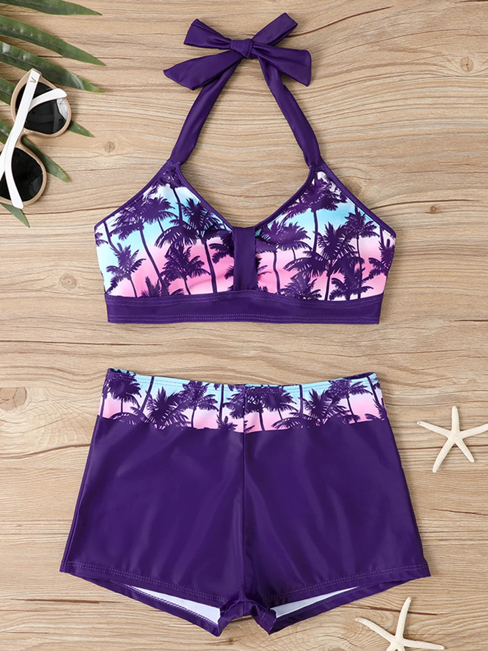 Tidesmit high-waisted bikini in purple with a blue-pink palm tree print, halter neck top, and boy-short bottoms.