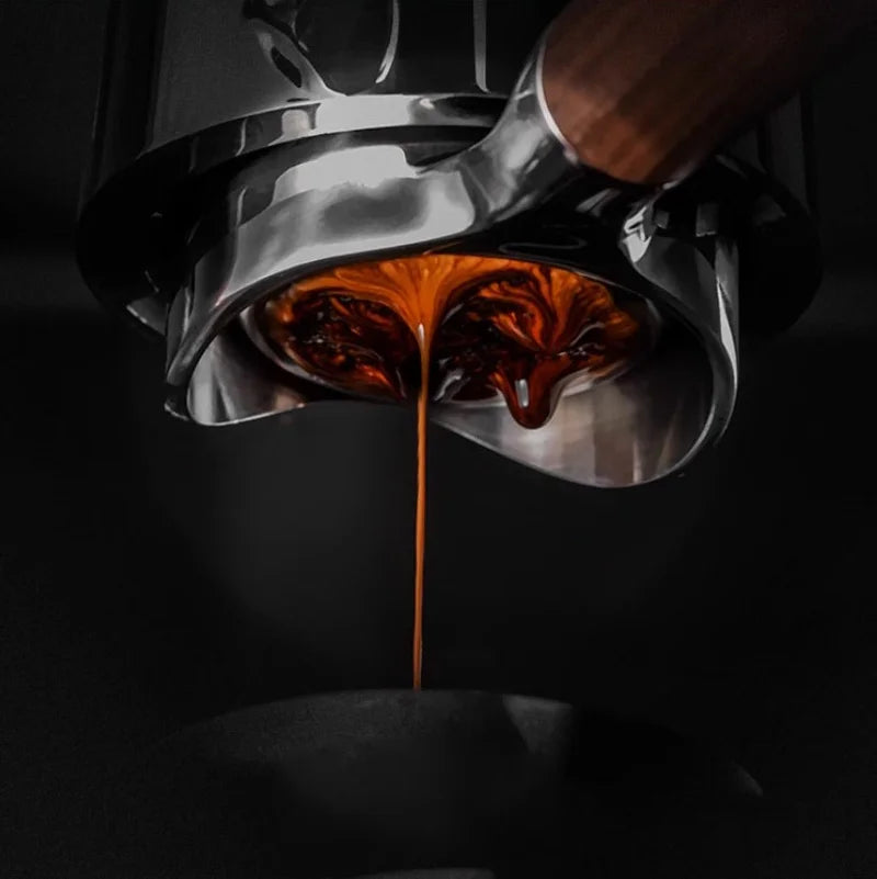 Espresso extracting from a stainless steel bottomless portafilter with a polished finish and wooden handle.
