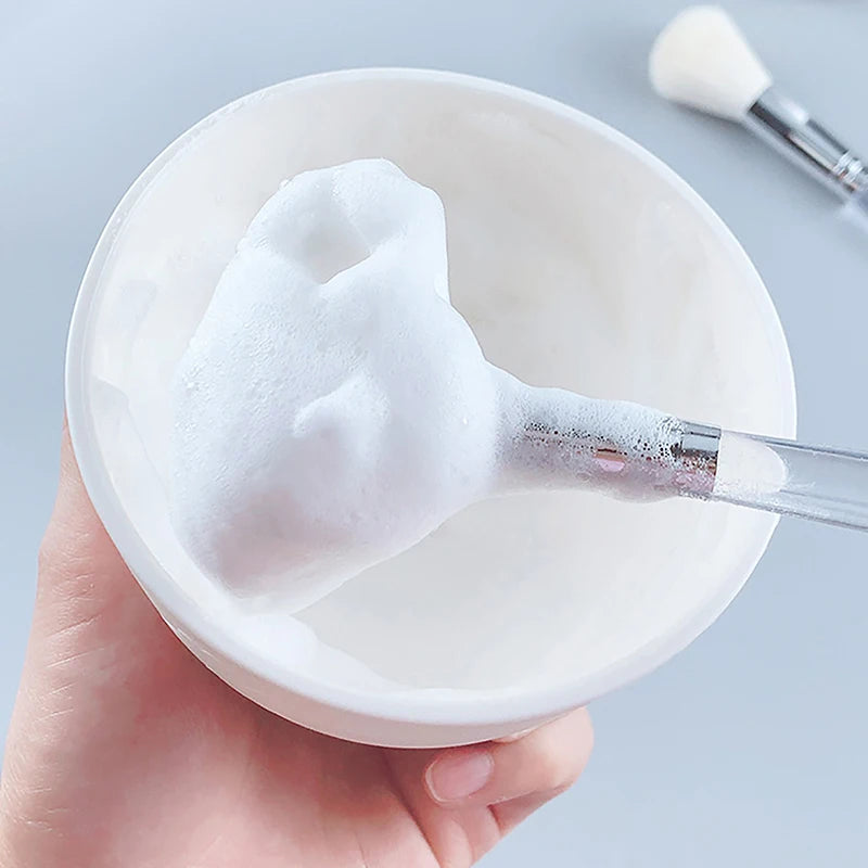 Soft facial cleanser brush with fluffy white foam, held in hand for gentle skin care and face mask application.
