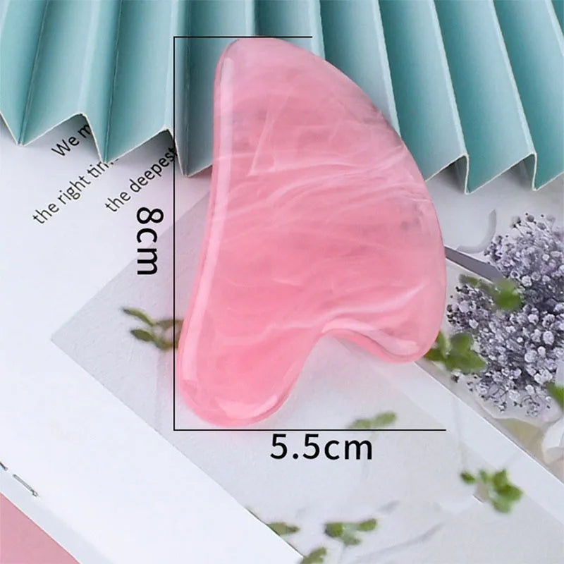 Pink heart-shaped resin gua sha massage tool measuring 8cm by 5.5cm, shown on a decorative surface.