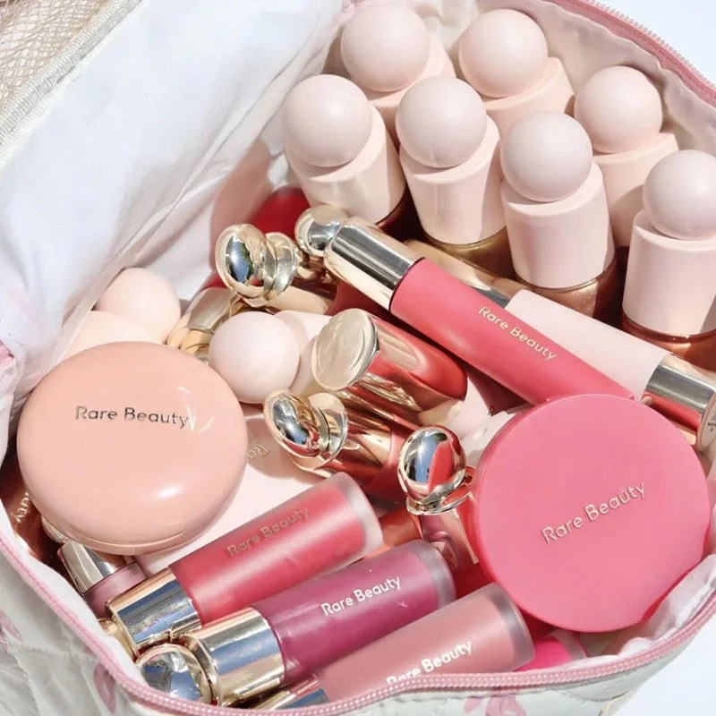 Rare Beauty makeup collection in a pouch: liquid blush, silky highlighter, and luminizers in shades of pink and rose.