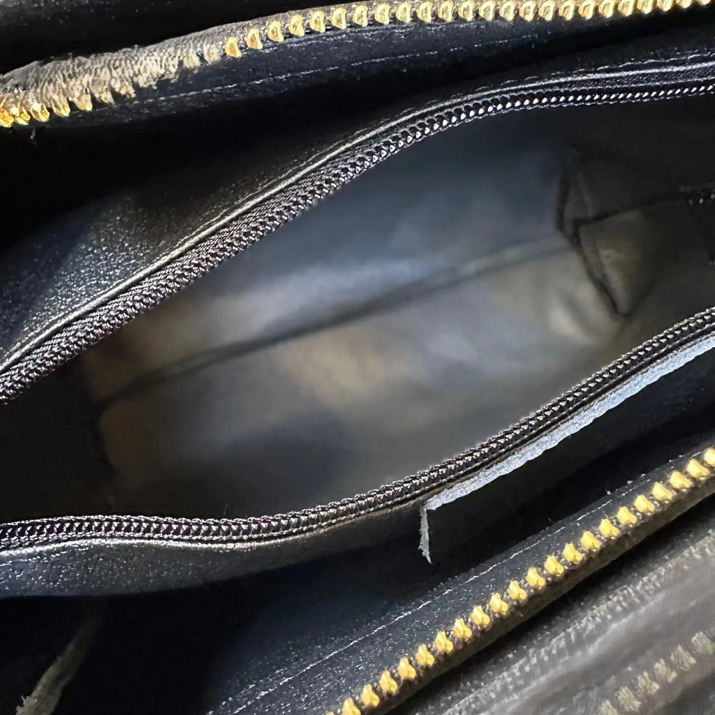 Interior of black handmade genuine leather designer tote bag with polyester lining and gold-tone zipper compartments.