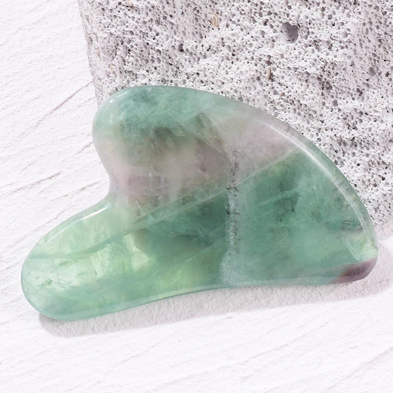 Smooth, heart-shaped green jade gua sha facial massage tool resting on a textured gray stone surface.