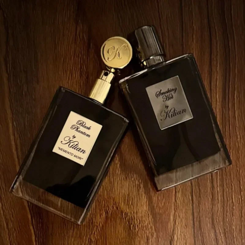 Kilian Black Phantom and Smoking Hot unisex eau de parfum bottles with elegant black glass and gold accents on wood.