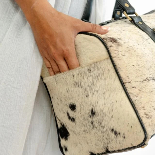 Genuine leather cow hair-on-hide weekender trunk bag with black leather trim and portable side pocket.