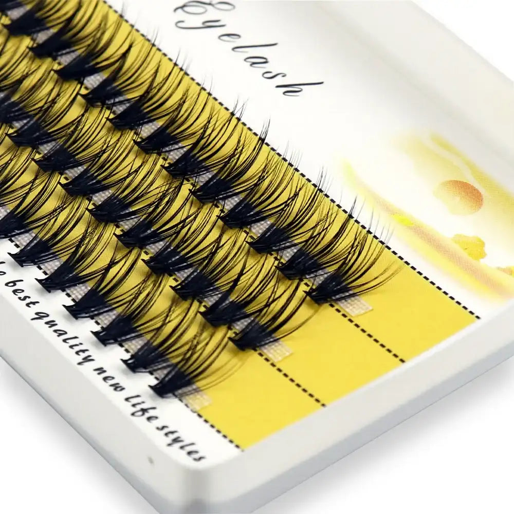 A box of black, wispy 3D individual mink eyelash clusters arranged on a bright yellow, branded display tray.
