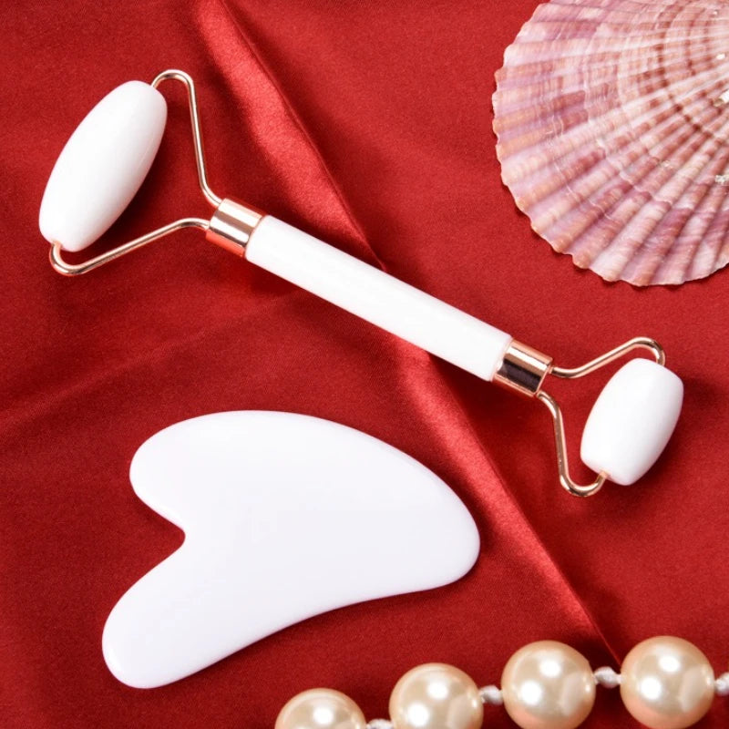 White resin facial roller and gua sha scraping tool set for anti-aging skin massage on red silk background.