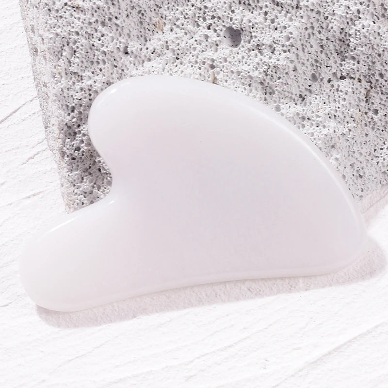 White heart-shaped stone gua sha facial massage tool resting on a textured gray rock background.