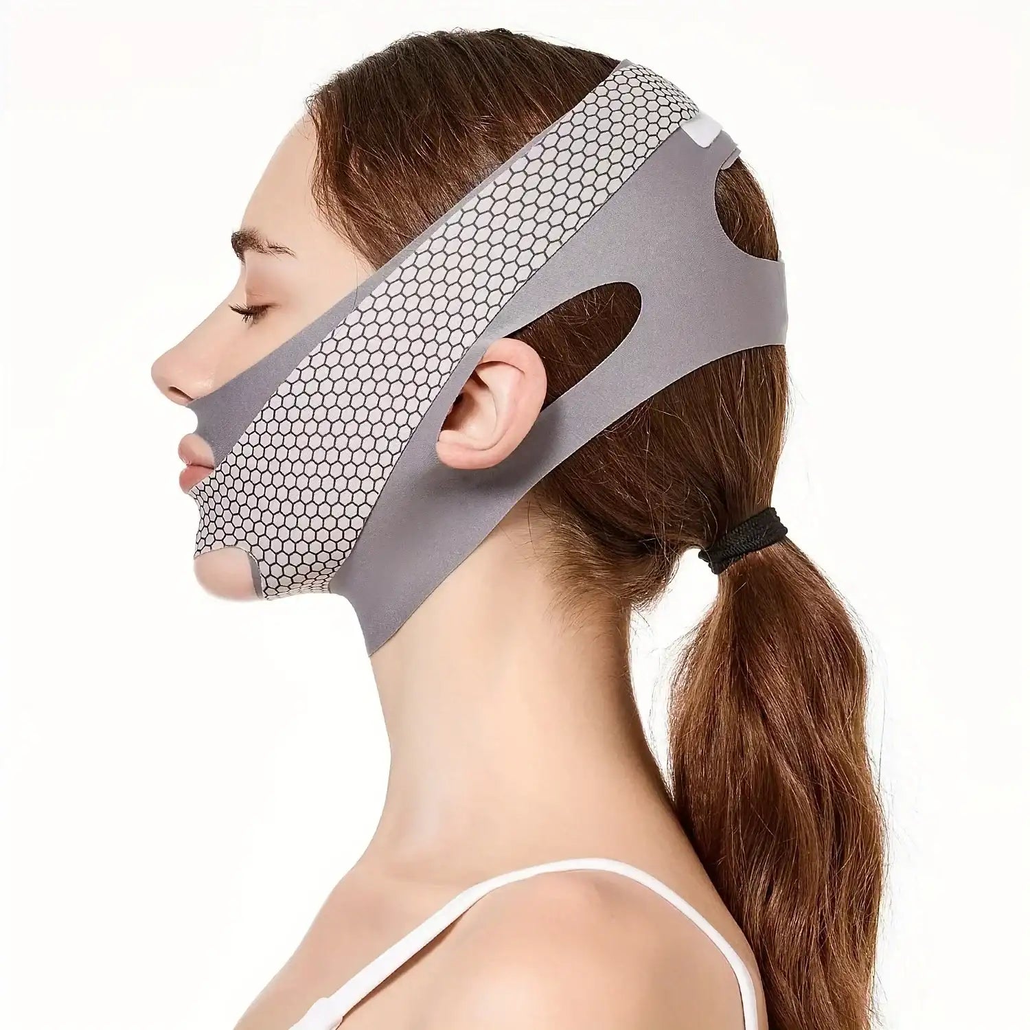 Profile view of a woman wearing a gray, honeycomb-textured V-line face slimming bandage with ear cutouts.