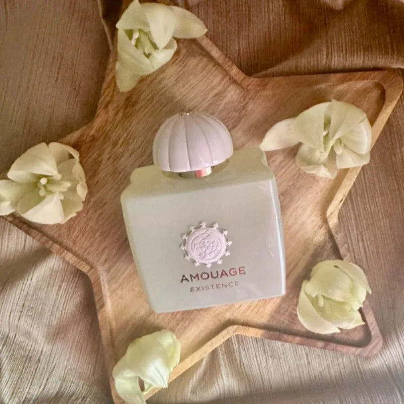 Amouage 100ml pale green perfume bottle with a dome cap, displayed on a wooden star tray with white flowers.