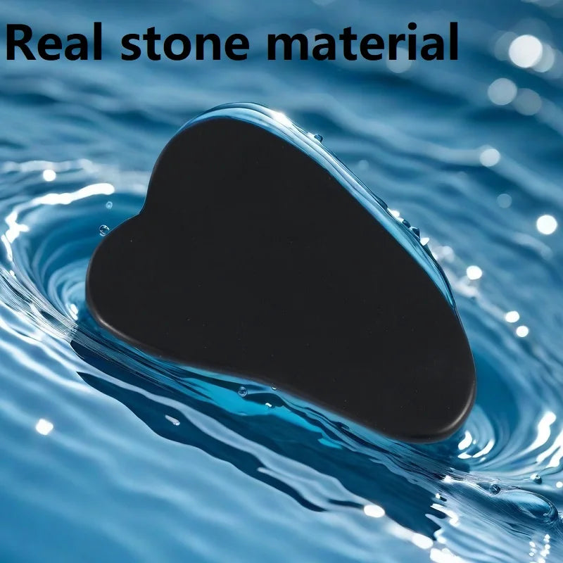 A black, heart-shaped stone gua sha tool resting on rippling blue water.
