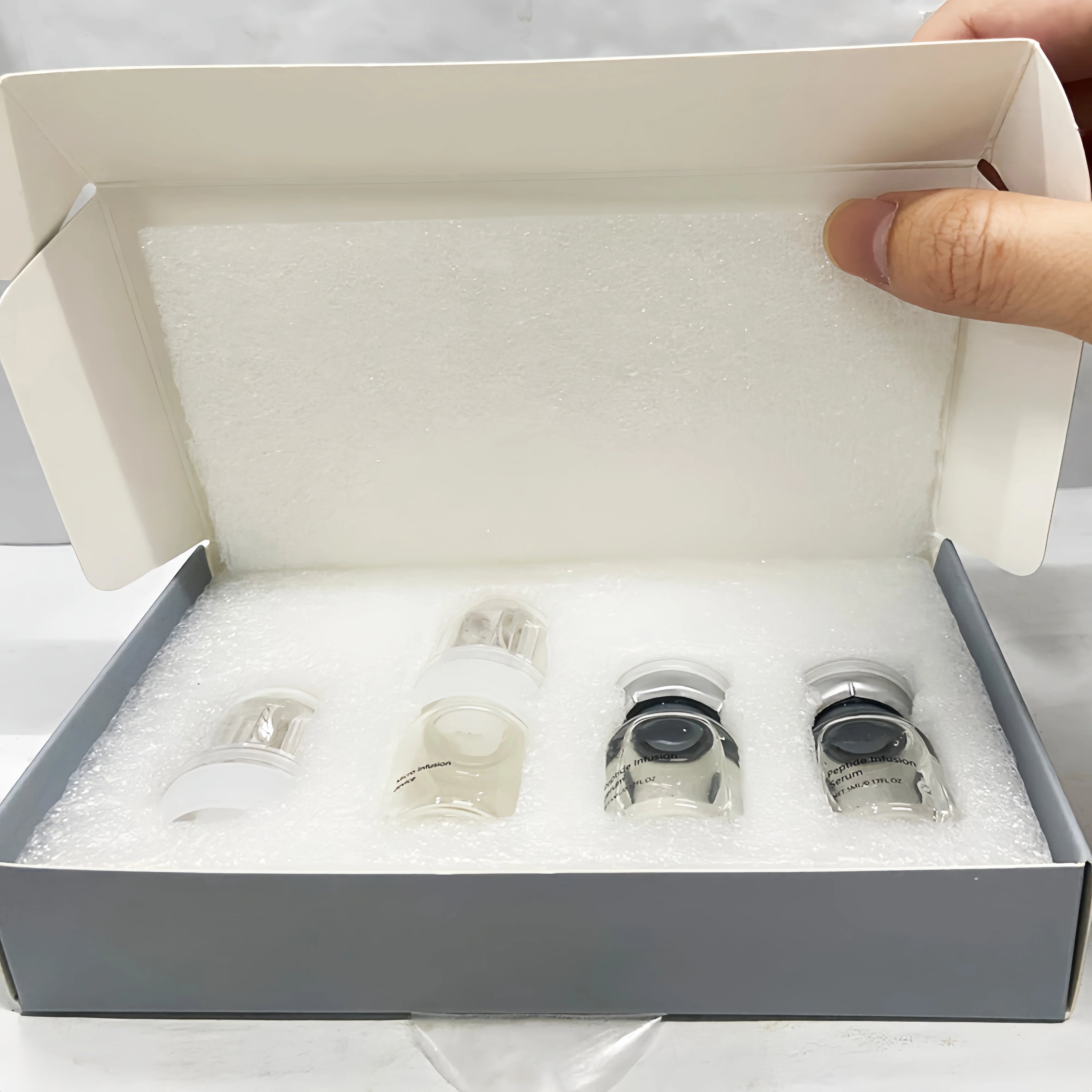 Open box containing four small, clear glass serum vials in a white foam insert.