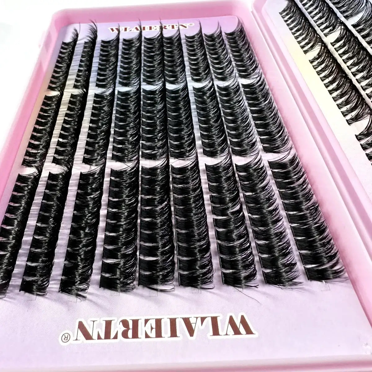Rows of individual black false eyelash clusters arranged in a pink plastic case for makeup application.