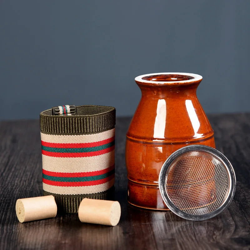 Brown ceramic moxibustion cup with a mesh filter, an elastic striped sleeve, and two small wooden pegs on a table.