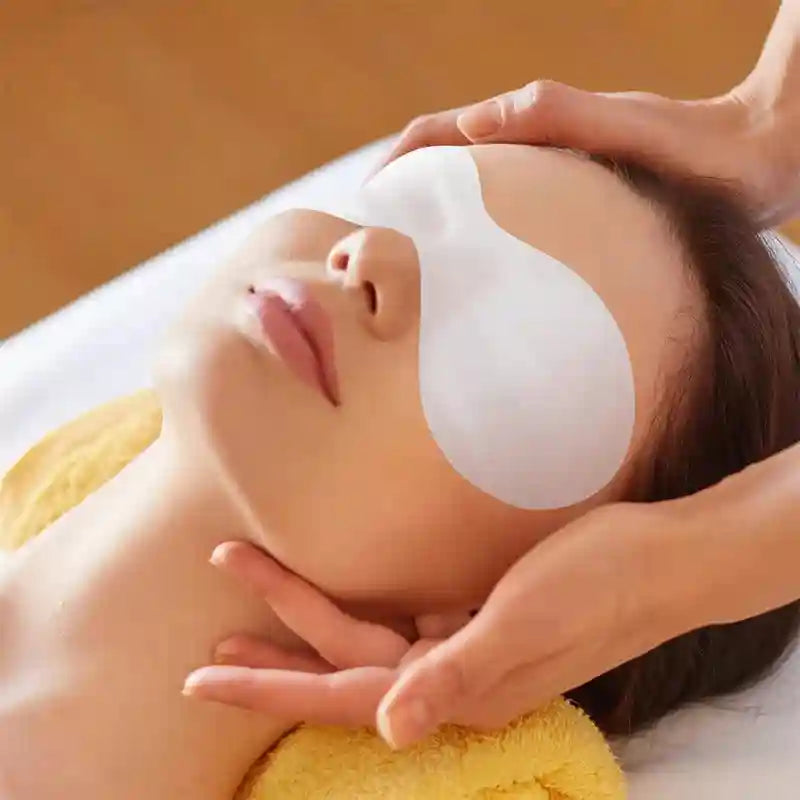 A person receiving a spa treatment with a white, disposable, ultrathin cotton eye mask covering their eyes.